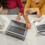 Two professionals engage in a collaborative discussion with laptops and coffee at a modern workspace. — Challenges to Overcom