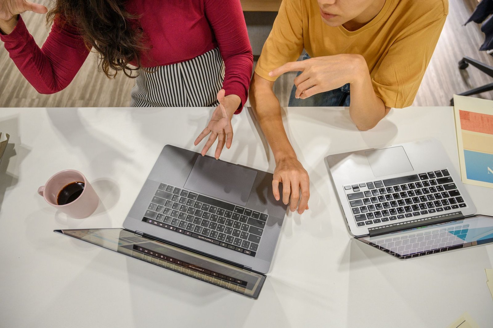 Two professionals engage in a collaborative discussion with laptops and coffee at a modern workspace. — Challenges to Overcom